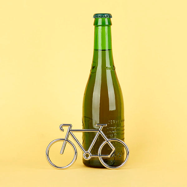 Botellín de cerveza verde junto a un abridor con forma de bicicleta