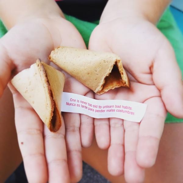Manos de niño con una galleta de la fortuna partida y un papelito con mensaje: "Nunca es tarde para perder malas costumbres"