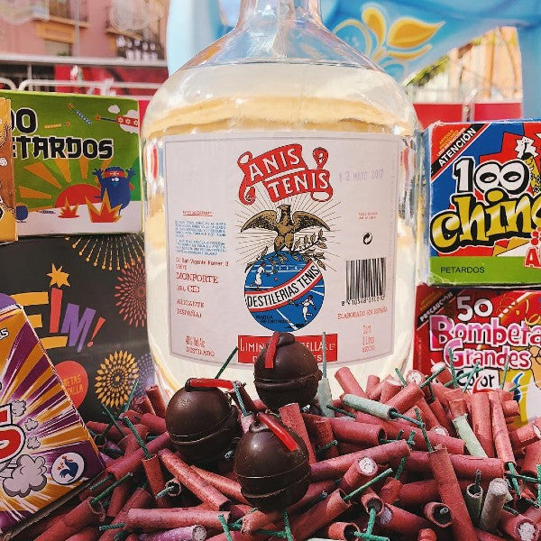 Bombones de chocolate rellenas de cazalla con mecha de regaliz sobre un montón de masclets y delante de una garrafa de Anís Tenis y cajas de Chinos y Tracas, explosivos típicos de las Fallas de Valencia