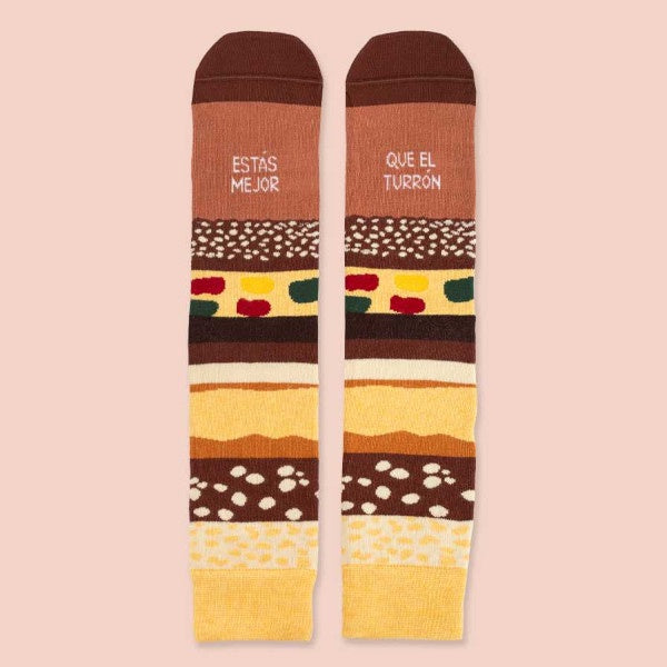 Calcetines de Navidad estampados de capas de chocolate, almendra, fruta escarchada, almendrado, turrón blando y el mensaje "Estás mejor que el turrón"