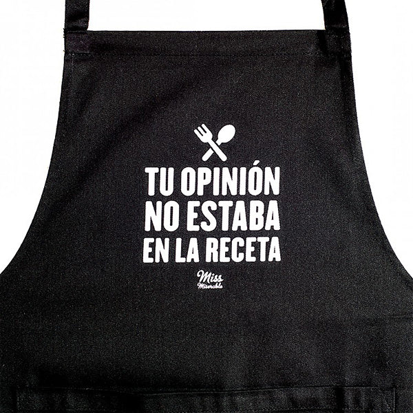 Primer plano del delantal de tela negro con bolsillo y el mensaje "Tu opinión no estaba en la receta"