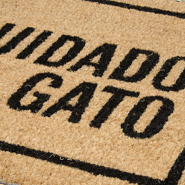 Primer plano de un felpudo de fibra de coco en marrón con texto negro "Cuidado con el gato" y la silueta de un gato enfadado