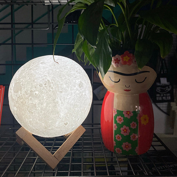 Lámpara luna mediana con base de madera con un jarrón con forma de Frida Kahlo al lado