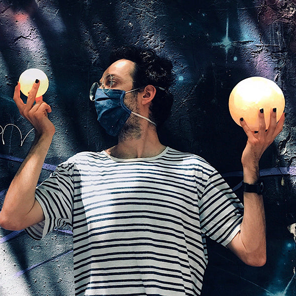 Hombre sujetando dos lámparas con forma de luna sobre fondo de graffiti de galaxia