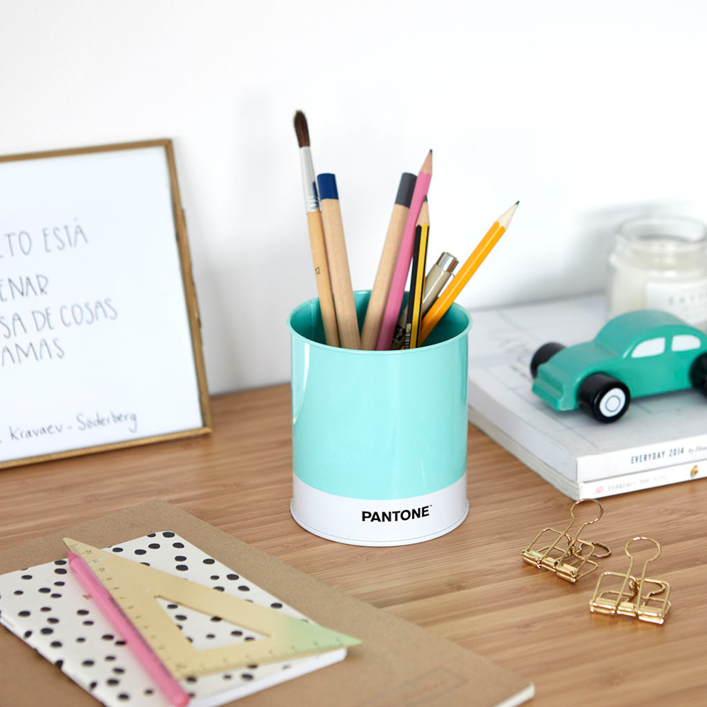 Escritorio con varios artículos de papelería y lápices, bolígrafos y pinceles en un lapicero de lata pantone azul celeste