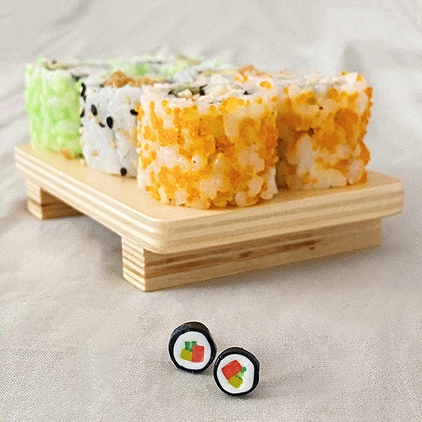 Mini pendientes con forma de maki junto a una bandeja de sushi
