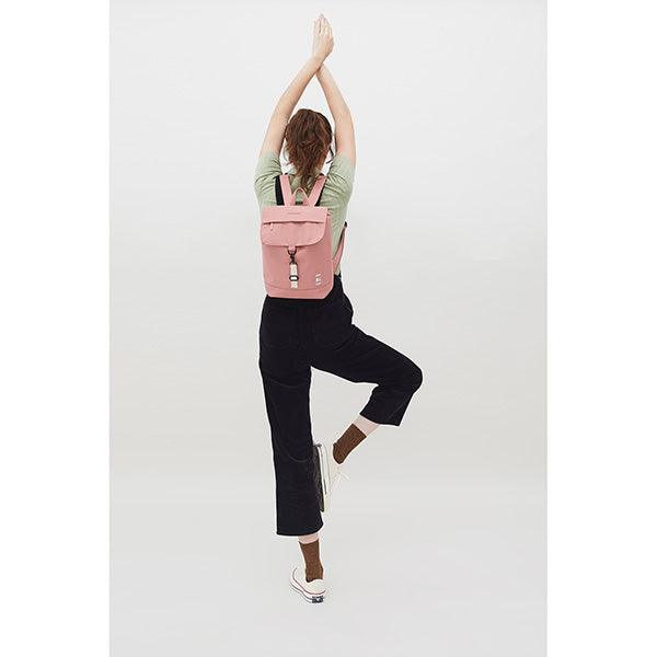 Mujer de espaldas haciendo la asana del árbol y una mini mochila rosa de Lefrik