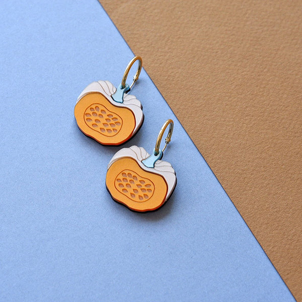Pendientes de aro de metacrilato con forma de calabaza partida sobre fondo azul y marrón