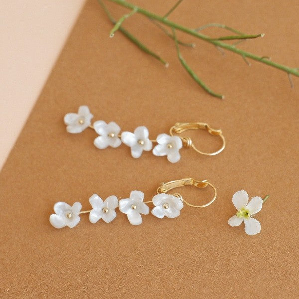 Pendientes largos con forma de ristra de florecillas blancas engastados sobre un palito dorado