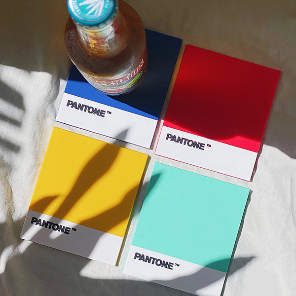 posavasos de colores Pantone con una bebida fría y la sombra de una palmera en verano