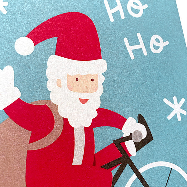 Detalle de papá noel montado en bici con copos de nieve y las palabras Ho ho ho