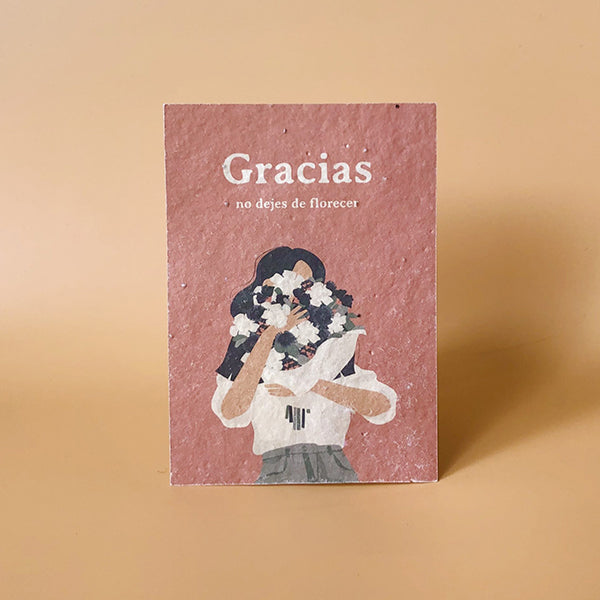 Tarjeta postal ecológica con semillas Gracias de Sheedo con una mujer sosteniendo un ramo de flores blancas y el mensaje "Gracias No dejes de florecer"