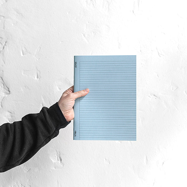 Una persona sostiene la libreta en tamaño A4, color azul e interior de rayas