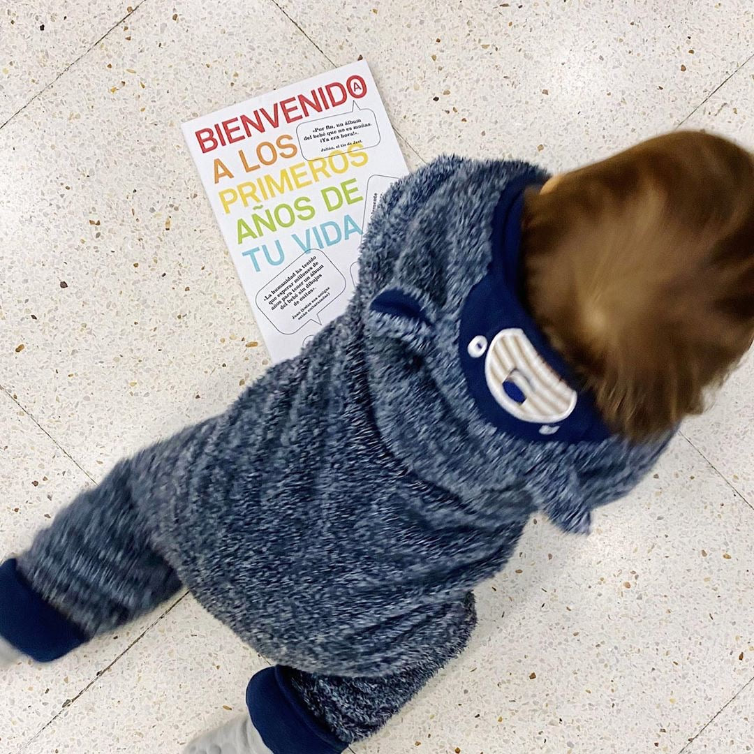 Bebé con pijama de peluche gateando sobre el diario del bebé Bienvenido a los primeros años de tu vida