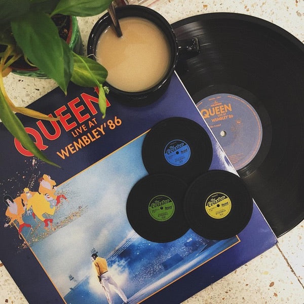 Posavasos con forma de disco de vinilo sobre un antiguo disco de Queen y una bebida al lado