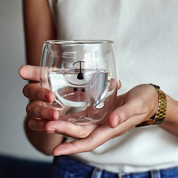 Una persona sujeta el vaso de cristal con forma y cara de oso lleno de agua.