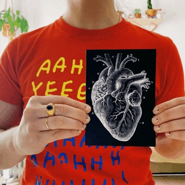 Chica sujetando entre las manos una tarjeta negra con un corazón anatómico blanco