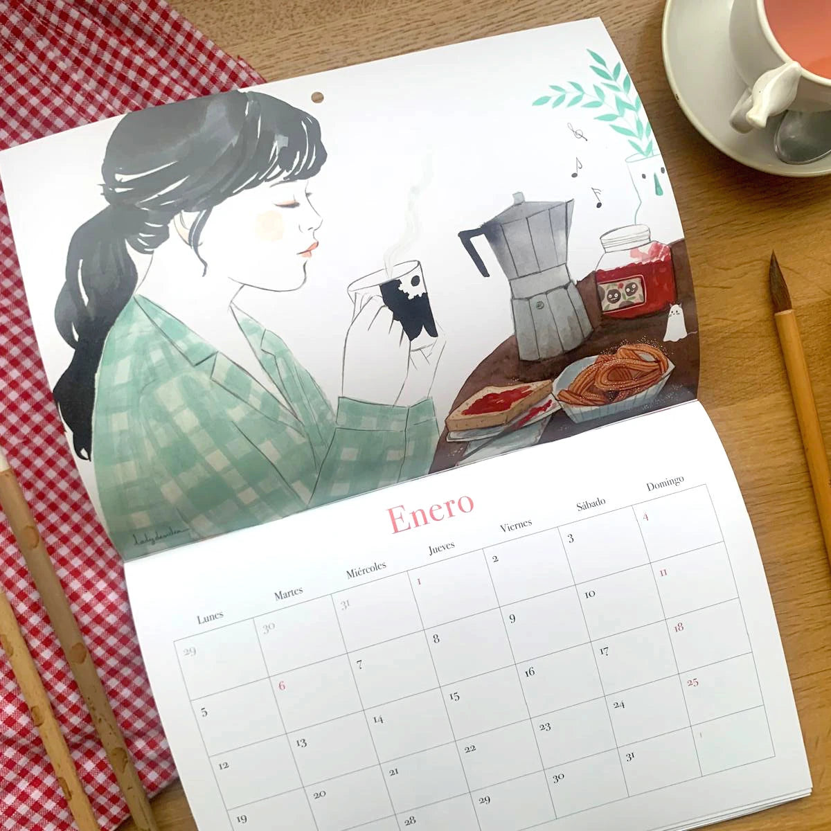 Diseño del mes de enero del Calendario de pared 2026 de Esther Gili, Marialu Gili y Lady Desidia con una chica bebiendo café con unas tostadas y churros ilustrada por Lady Desidia