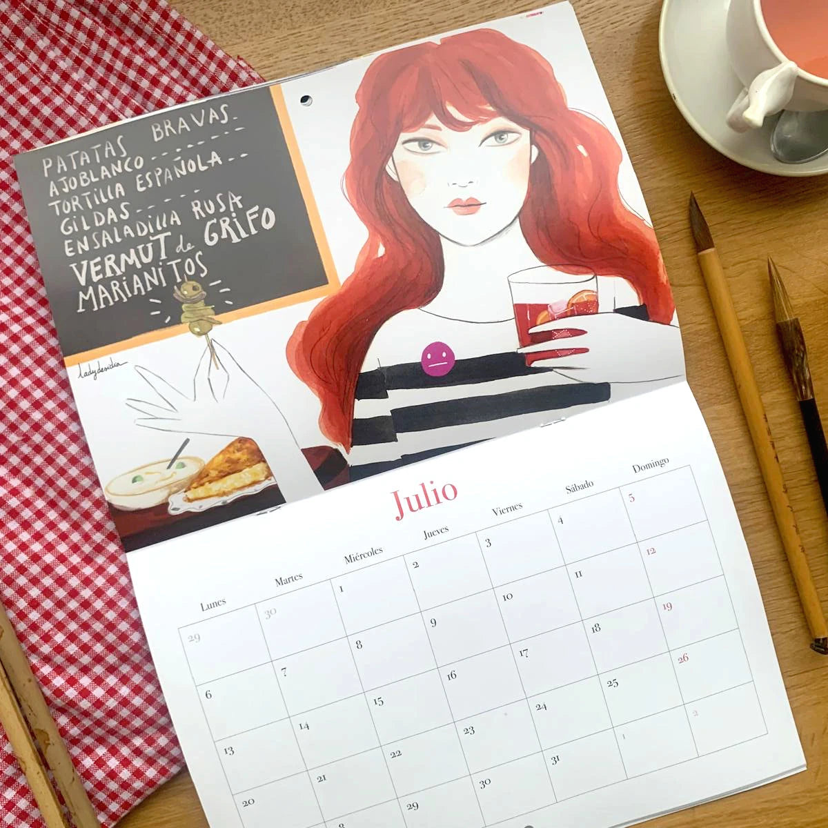 Diseño del mes de julio del Calendario de pared 2026 de Esther Gili, Marialu Gili y Lady Desidia con ilustración de Lady Desidia de una chica tomando pinxos y vermout en un bar