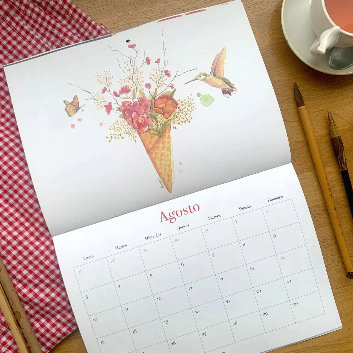 Diseño del mes de agosto del Calendario de pared 2026 de Esther Gili, Marialu Gili y Lady Desidia con ilustración de Marialu de un cucurucho lleno de flores y un colibrí y una mariposa