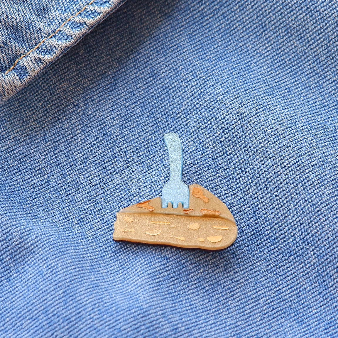 pin de un pincho de tortilla en metacrilato con un tenedor pinchandolo colocado en una chaqueta vaquera