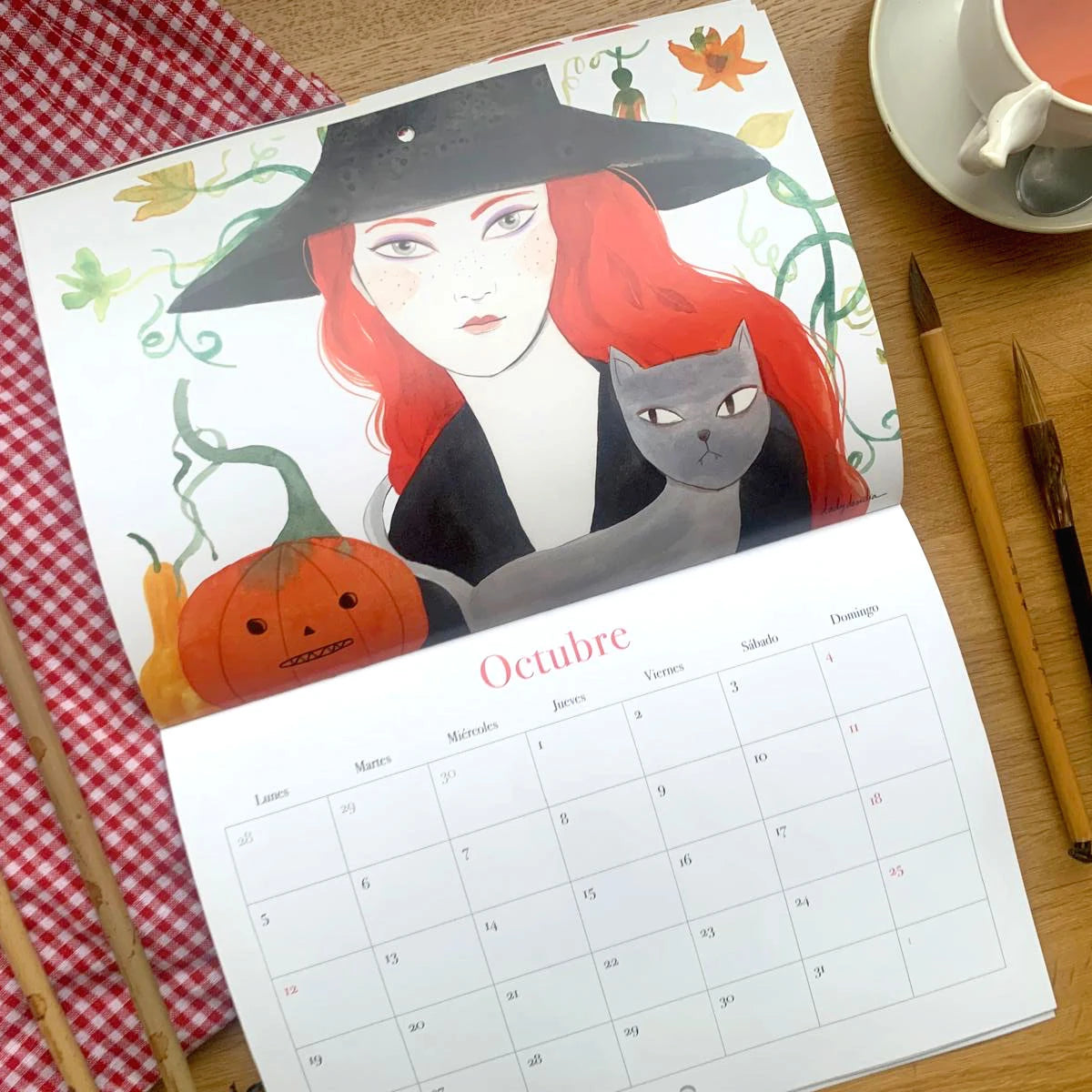 Diseño del mes de octubre del Calendario de pared 2026 de Esther Gili, Marialu Gili y Lady Desidia con ilustración de Lady Desidia de una brujacon un gato y una calabaza