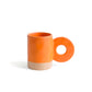 taza de cerámica de color naranja de Helio Ferretti con la base de color beige, con asa grande en forma de círculo 