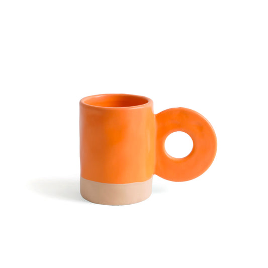 taza de cerámica de color naranja de Helio Ferretti con la base de color beige, con asa grande en forma de círculo 