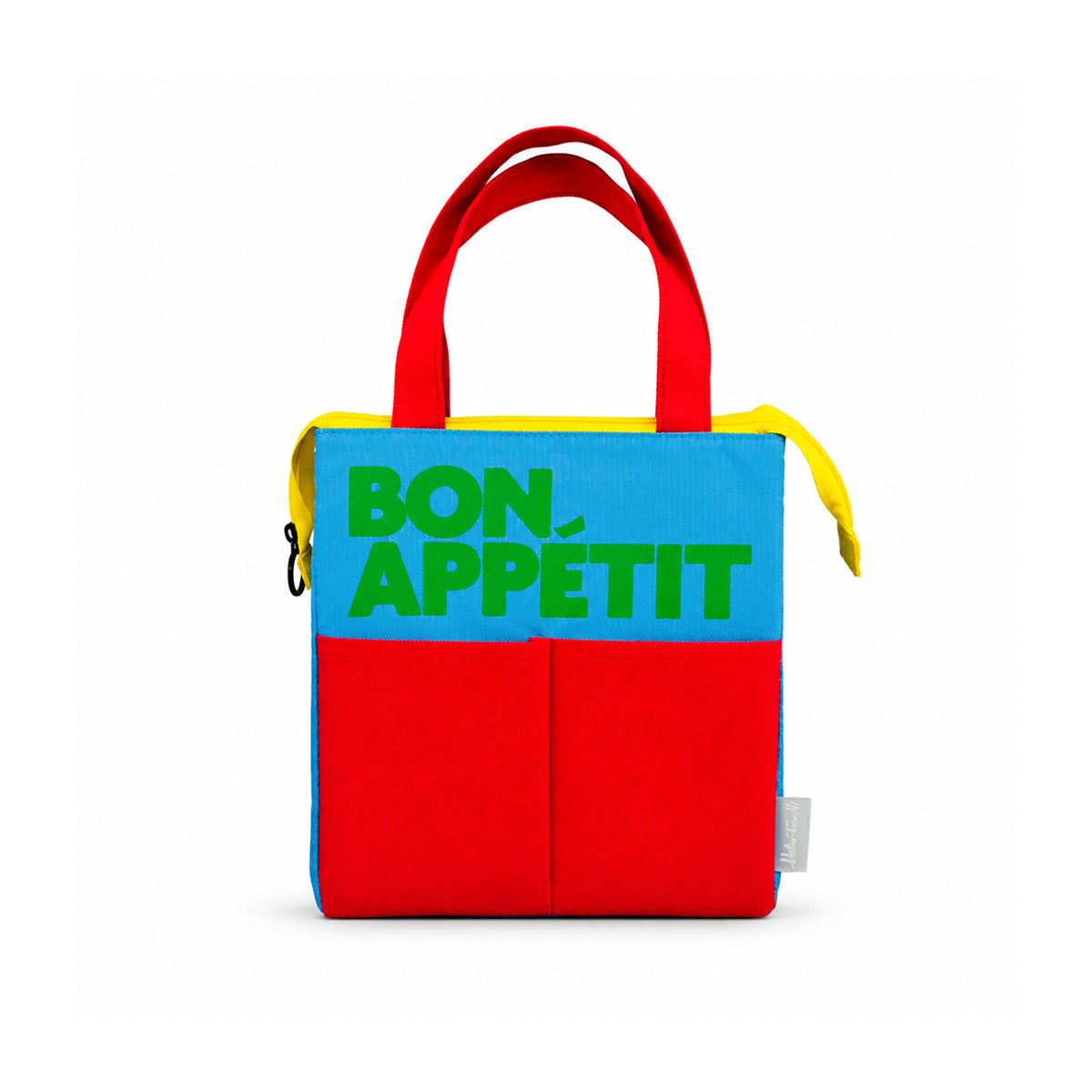 Bolsa isotérmica azul de Helio Ferretti con mensaje «Bon Appétit» en verde, asas rojas, dos bolsillos frontales rojos y cremallera amarilla.
