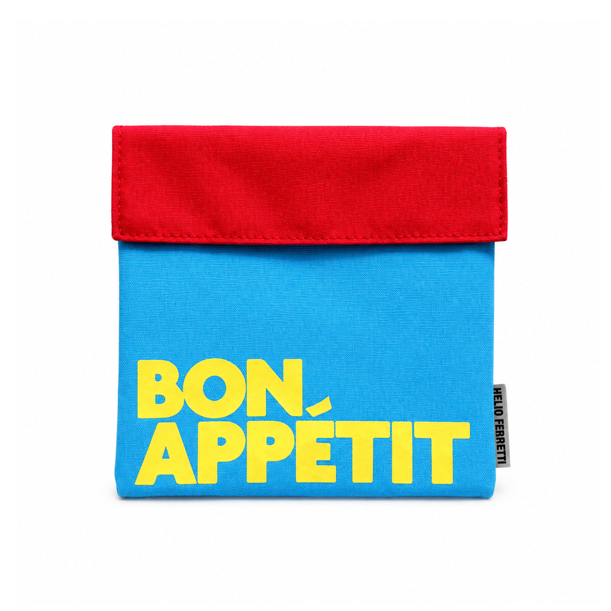 Bolsa de almuerzo azul de Helio Ferretti con solapa roja y mensaje «Bon Appétit» en letras amarillas, sobre fondo blanco.

