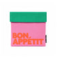 Bolsa de almuerzo Bon Appétit de Helio Ferretti en rosa, con solapa verde y letras naranjas, vista frontal.
