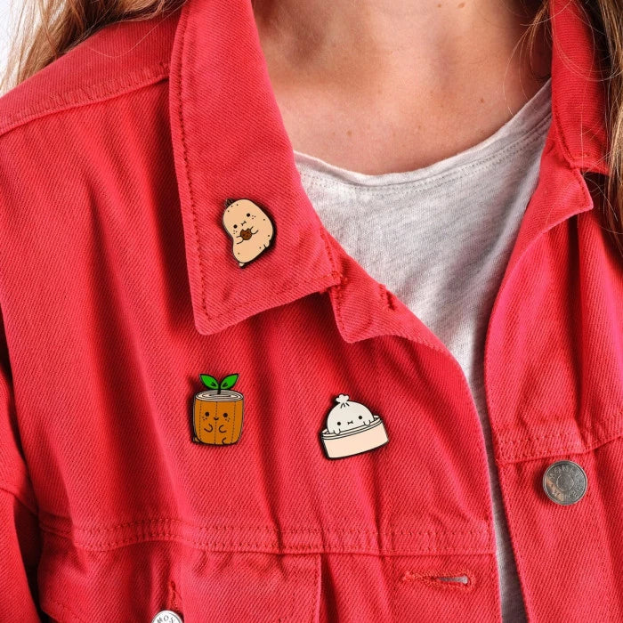 Pin kawaii de Noodoll con diseño de pan bao en vaporera puesto en una chaqueta roja junto con otros pins. 