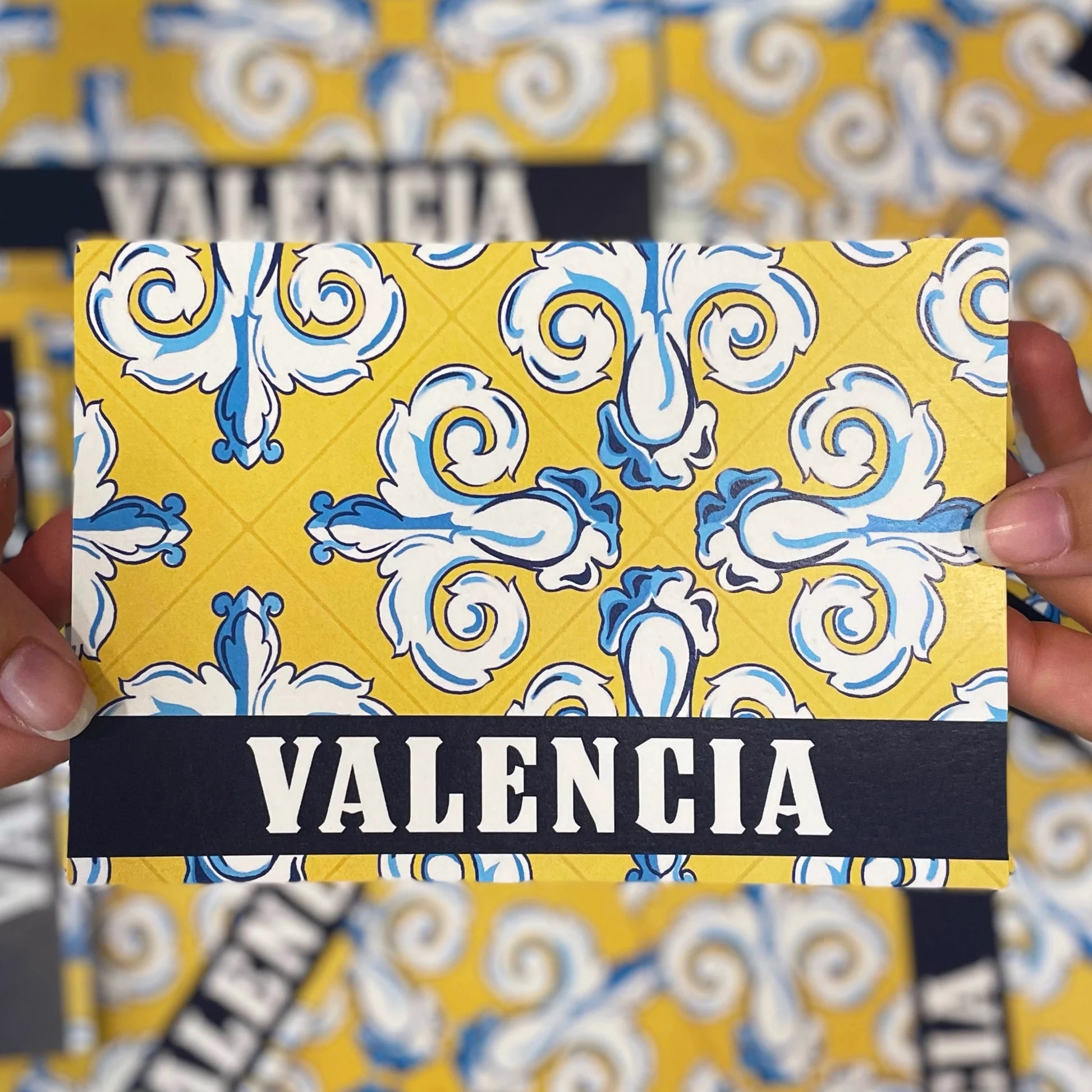 Postal con dibujo de azulejos color amarillo con detalles en azul y blanco con letrero negro y blanco de Valencia de Laura Ortiz