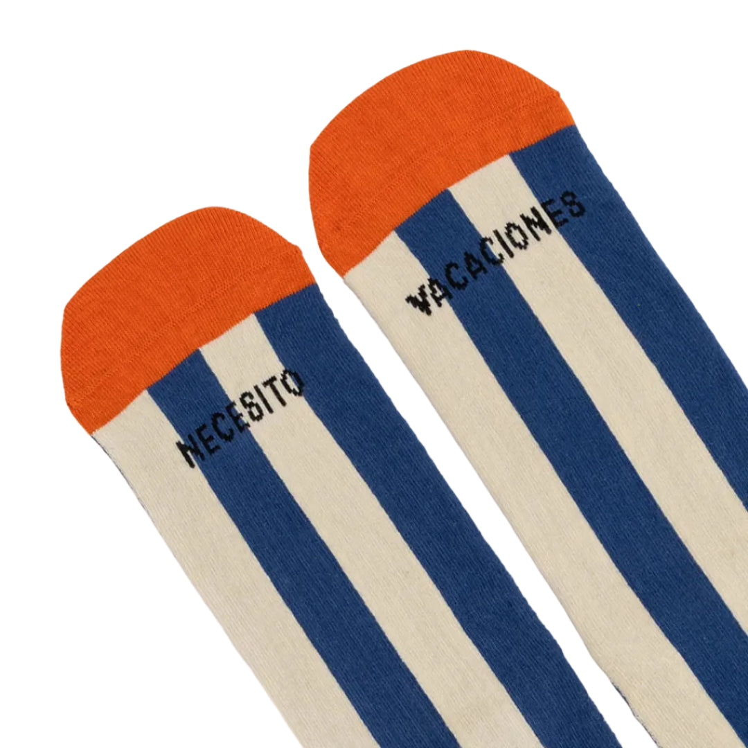 Detalle de la puntera de los calcetines a rayas verticales azules y puntera naranja con dibujo de un sol y el texto "Necesito vacaciones"