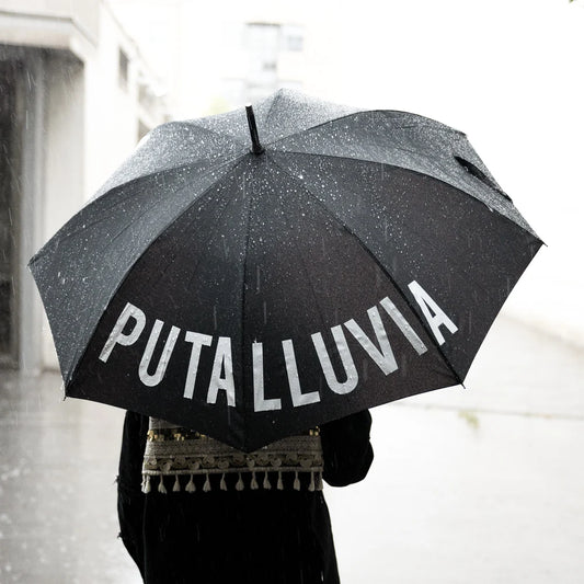 persona de espaldas con un paraguas en color negro con el texto "PUTA LLUVIA" en blanco mientras llueve
