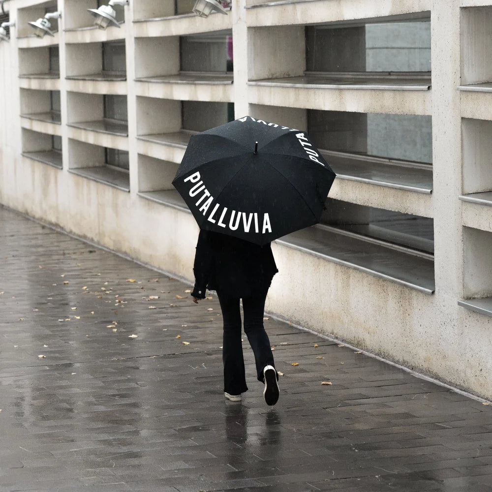 persona camiando por la calle de espaldas con el paraguas de Fisura Puta lluvia escrito en la parte de delante y en la de detrás