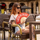 Chica sentada en una silla aguantando el abanico con el texto "Cazzo di caldo".