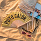 abanico de la marca fisura con purpurina dorada y el texto "PUTO CALOR" en color negro, sobre una toalla en la playa al lado de una bolsa y unas gafas de sol