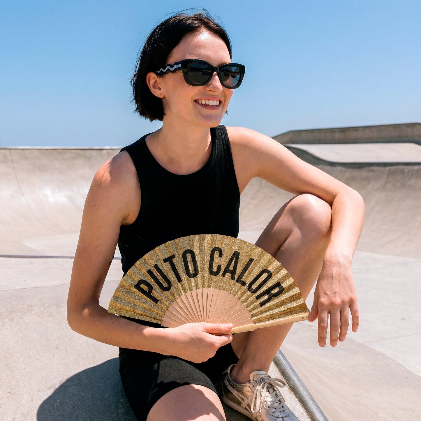 chica con el abanico de la marca fisura con purpurina dorada y el texto "PUTO CALOR" en color negro y las gafas de sol dolce vita