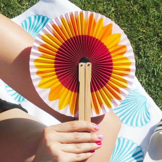 persona sujetando el paipai plegable redondo de papel con estampado de un girasol sobre una toalla puesta en el césped