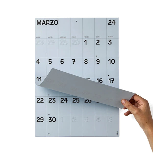 Mano levantando la página del mes de mayo del calendario de pared 2024 en papel azul y tamaño A3 en la hoja de enero de Colla Paper