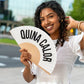 chica sujetando el abanico de fisura en color blanco de tela y madera con el texto en negro "QUINA CALOR" abierto