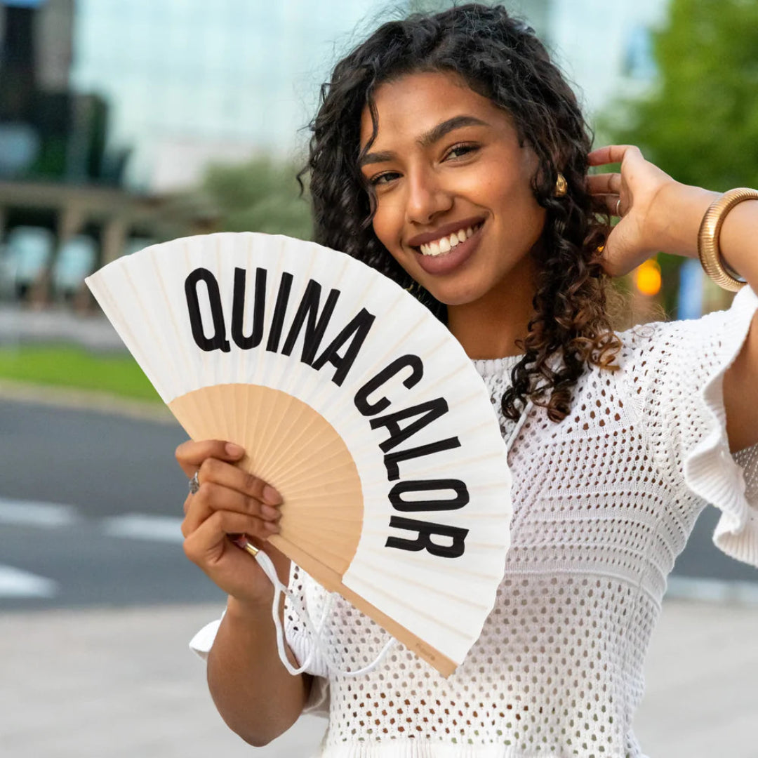 chica sujetando el abanico de fisura en color blanco de tela y madera con el texto en negro "QUINA CALOR" abierto