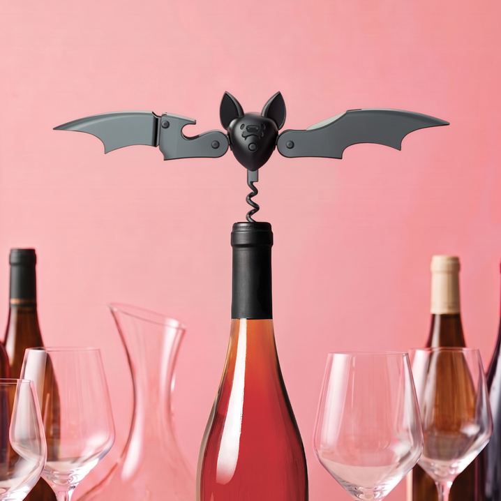Sacacorchos Murciélago de Ototo en color negro, con las alas extendidas sobre una botella de vino y fondo rosa.