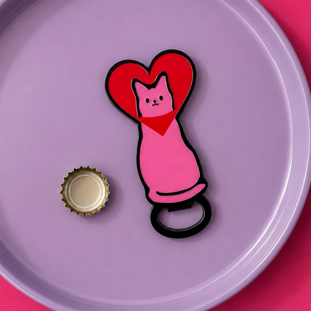 Abridor con forma de gato rosa con la cabeza metida en un corazón rojo encima de un plato lila