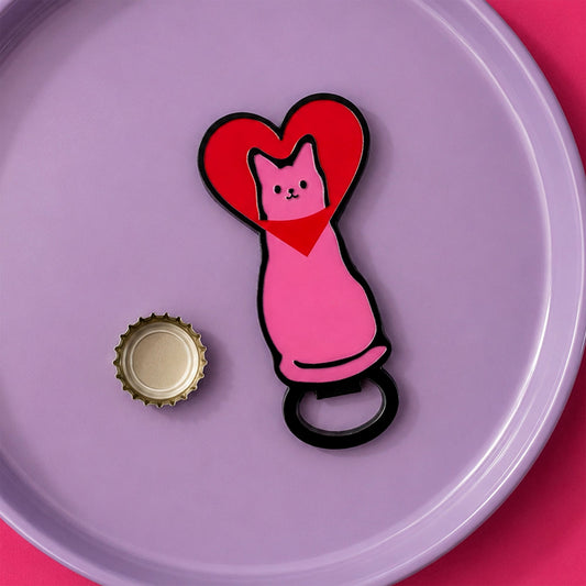 Abridor con forma de gato rosa con la cabeza metida en un corazón rojo encima de un plato lila