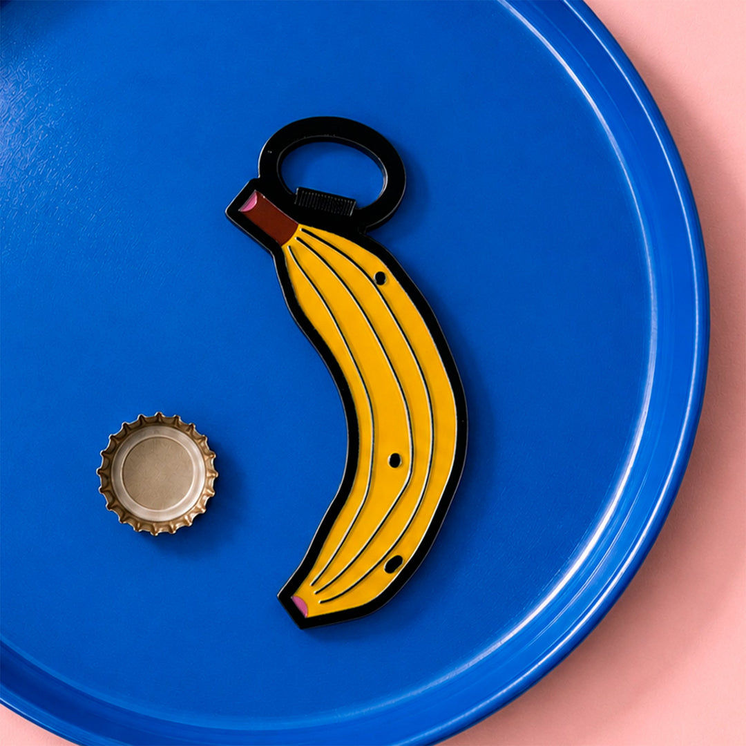 Abridor magnético con forma de banana sobre un plato azul junto a una chapa