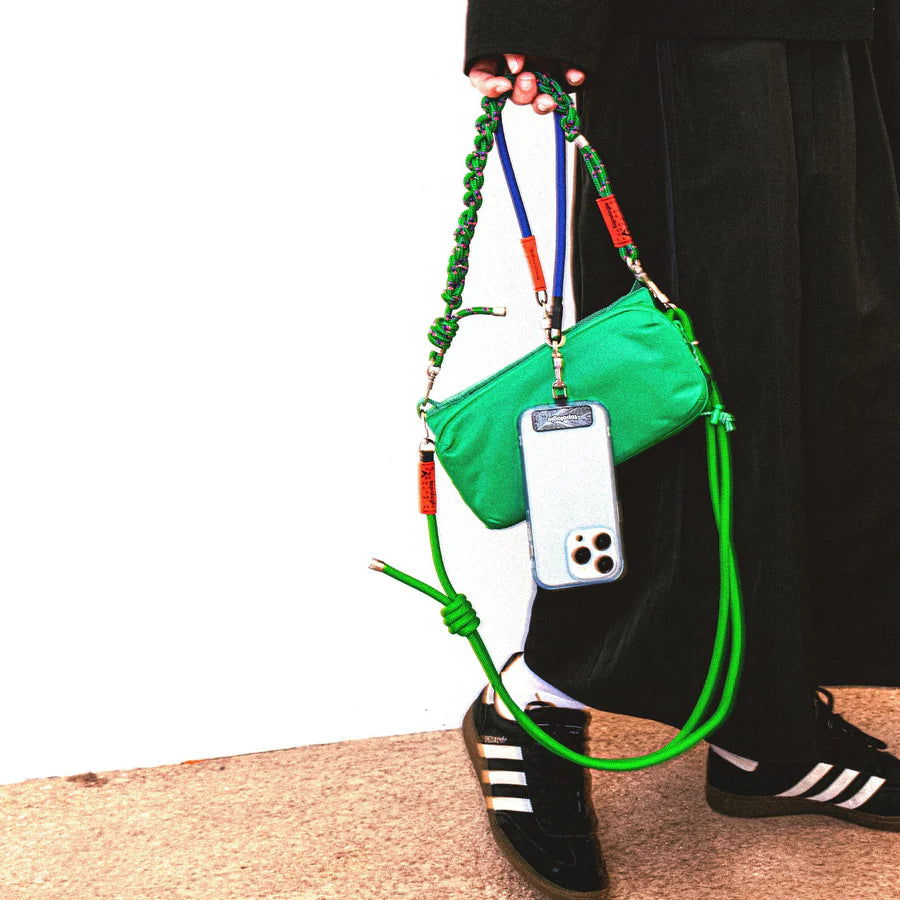 Chica con bolso verde de topologie y in móvil colgando de una correa con adaptador para enganchar correas al móvil de Topologie con gancho de acero inoxidable