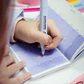 Mano escribiendo en agenda pocket Happimess con rotulador, mostrando la apertura flat-lay a 180°