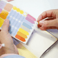 Manos despegando stickers de colores de la plancha incluida en la agenda Happimess Astro